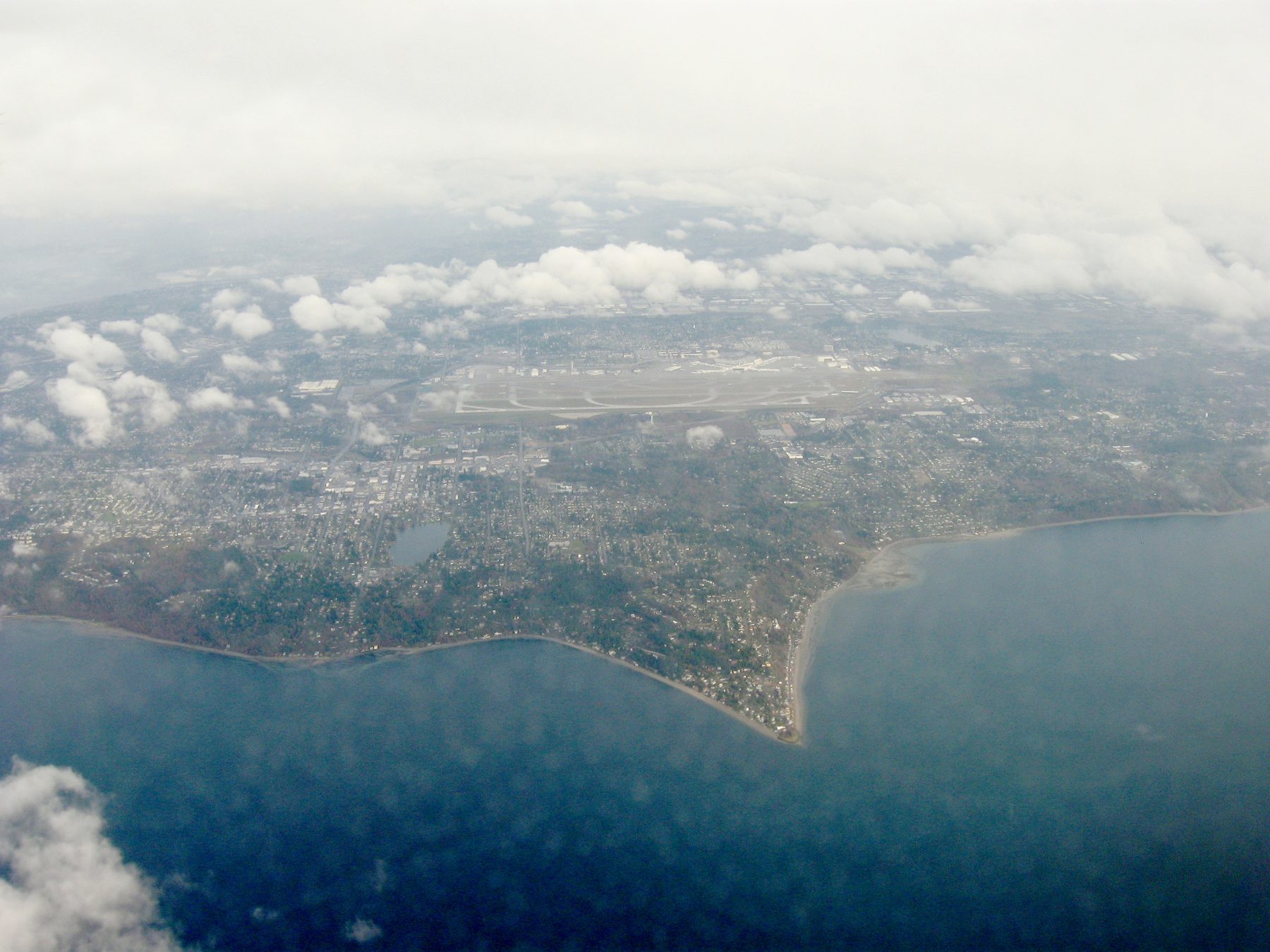 Aerial view of Three Tree Point, the triangle-shaped gravel spit jutting into Puget Sound at Burien, Washington, with SeaTac in the distance.